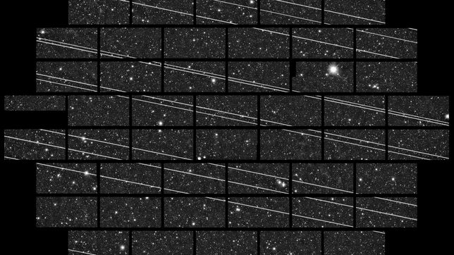 A telescope survey exposure crossed by many straight white satellite trails cutting diagonally across fields of stars
