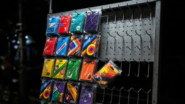 A night market rack of prepaid phone cards, most hooks stripped bare, one card caught falling away.
